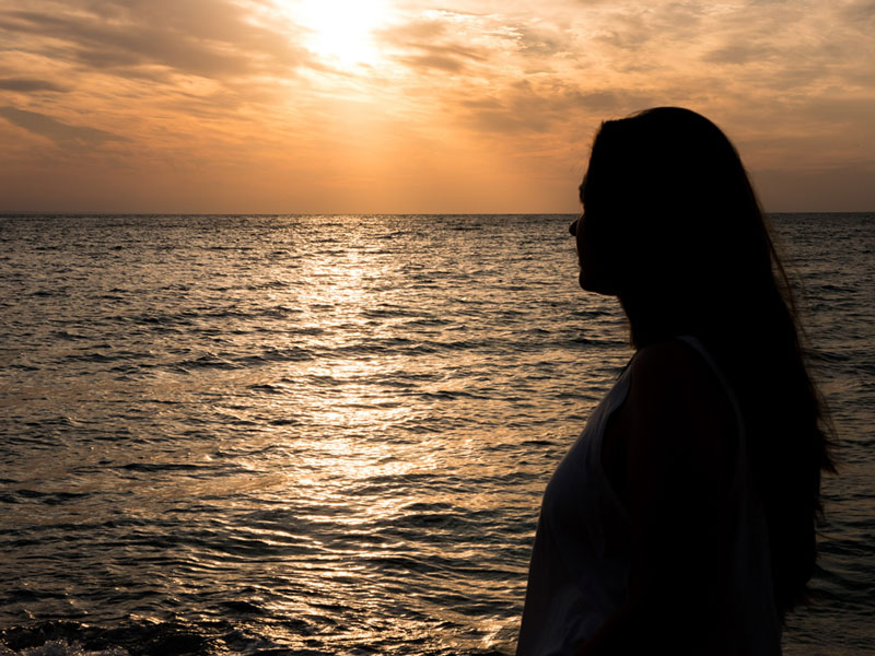 γυναίκα στην παραλία κοιτάζει το ηλιοβασίλεμα
