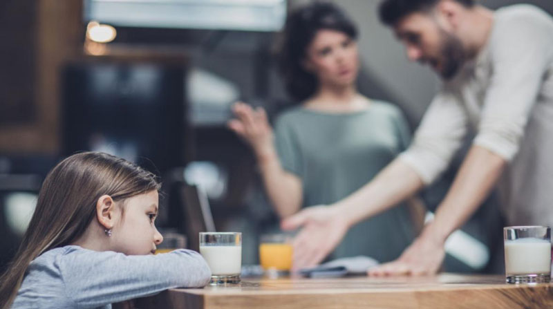 απογοητευμένο παιδί κάθεται στο τραπέζι ενώ οι γονείς διαφωνούν