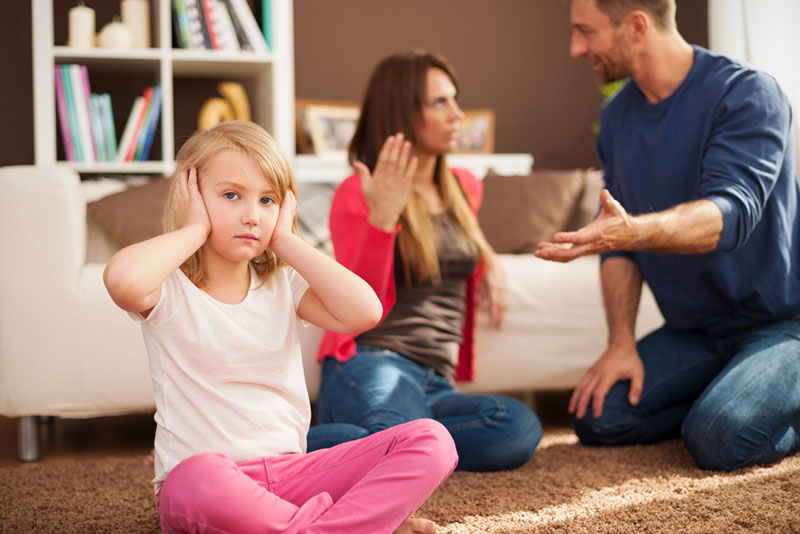 απογοητευμένο παιδί κάθεται με τα χέρια στα αυτιά ενώ οι γονείς διαφωνούν