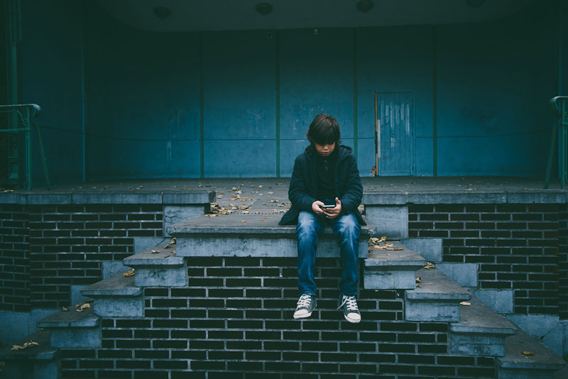 αγόρι πάσχει από συναισθηματική ορφάνια και κοιτάζει το κινητό του μιας έχει γονείς που δεν καλύπτουν τις συναισθηματικές του ανάγκες