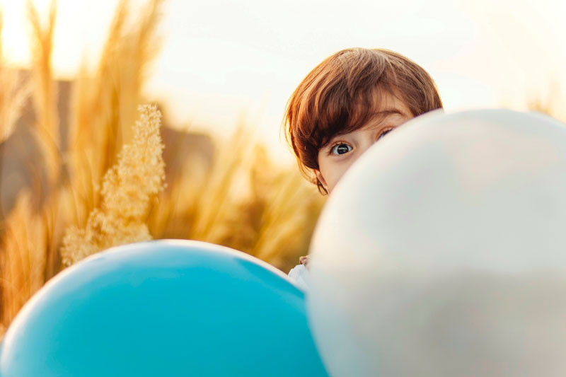 χαρούμενο παιδί κρύβεται πίσω από δύο μπαλόνια γεμάτο αυτοπεποίθηση