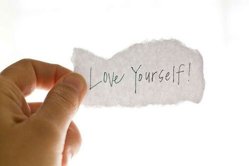 που κρατάει ένα χαρτί που γράφει love yourself