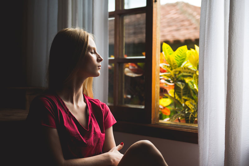 γυναίκα με κλειστά μάτια δίπλα στο παράθυρο σκέπτεται με το νου της