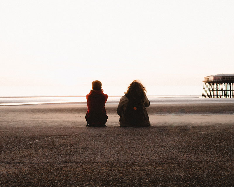 δύο άτομα κάθονται στην άμμο μιας παραλίας