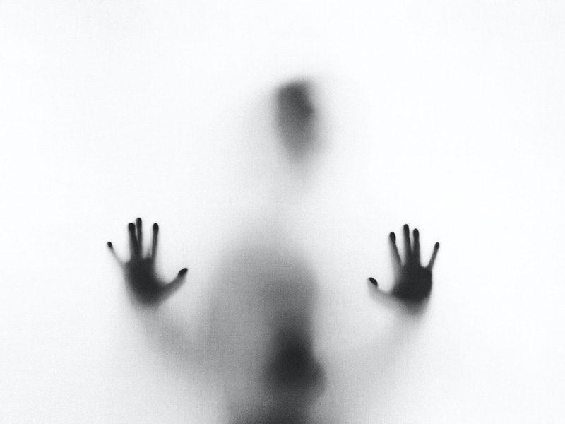 ασπρόμαυρη φωτογραφία ατόμου που ακουμπά τα χέρια της σε τζάμι που αντιμετωπίζει σιωπηρή κακοποίηση στην σχέση του
