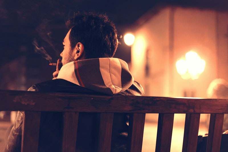 άντρας μόνος του καπνίζει σε ένα παγκάκι