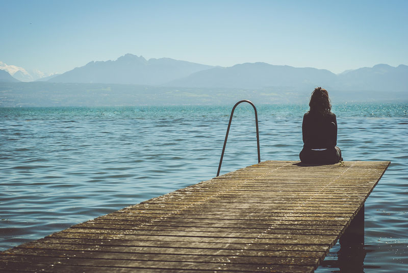 γυναίκα κάθεται μόνη της και περνάει χρόνο με τον εαυτό της, σε αποβάθρα και κοιτάζει τη θάλασσα