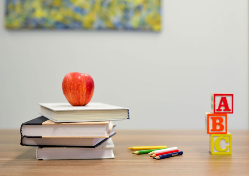 ένα θρανίο με ένα μήλο πάνω σε διάφορα βιβλία και χρωματιστά μολύβια