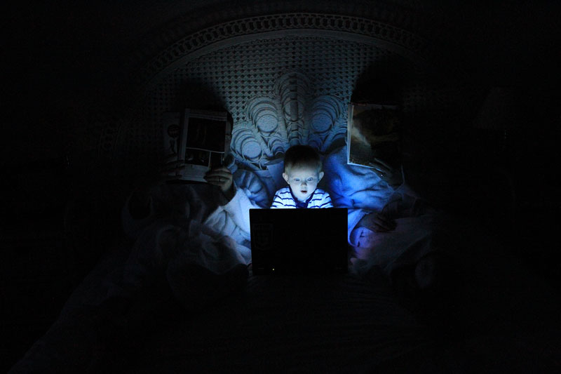 αγοράκι ξαπλωμένο στο κρεβάτι με γονείς που κρατά laptop