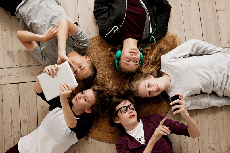 παρέα εφήβων ξαπλωμένη στο πάτωμα και κάνει χρήση των μέσων κοινωνικής δικτύωσης
