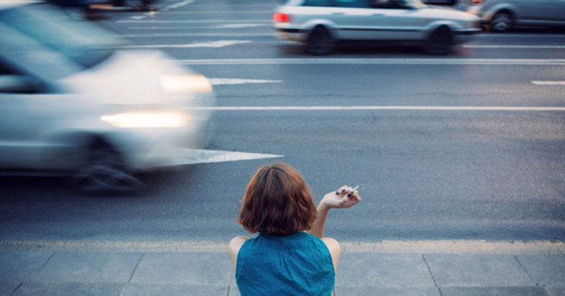 κοπέλα κοιτάζει το δρόμο με αυτοκίνητα κρατώντας τσιγάρο