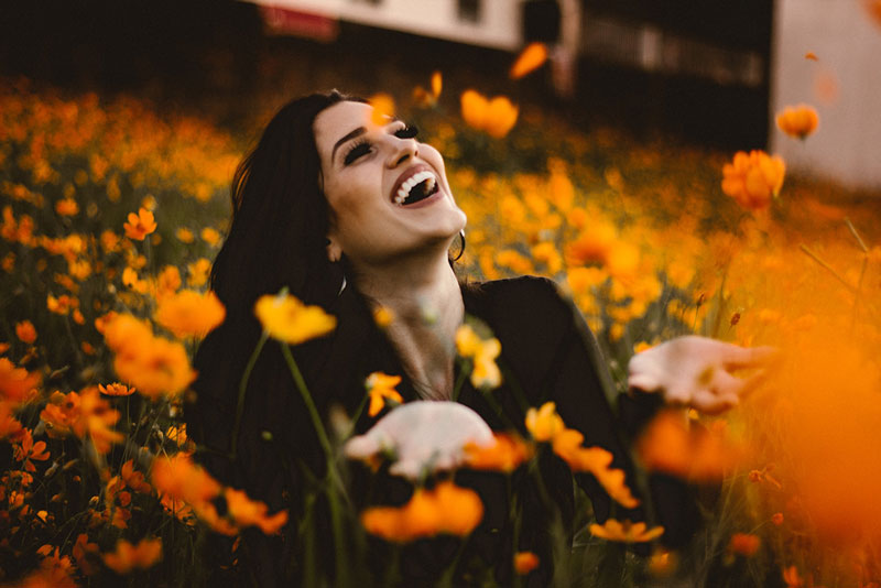 γυναίκα χαμογελάει σε λιβάδι με λουλούδια χωρίς να γνωρίζει τι σημαίνει ευτυχία