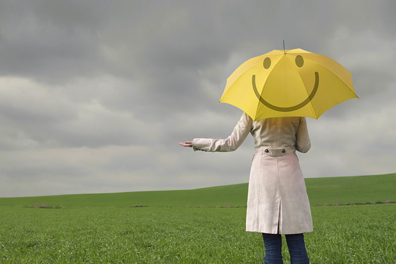 γυναίκα με παλτό που κρατά μία ομπρέλα με χαμόγελο