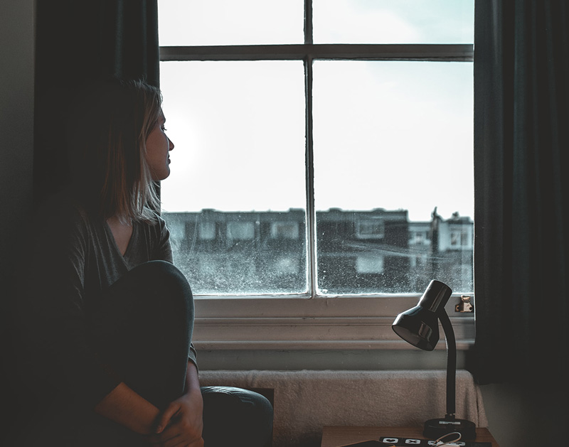 γυναίκα καθισμένη μπροστά από το παράθυρο διαχειρίζεται το άγχος και τα υπόλοιπα αρνητικά συναισθήματα
