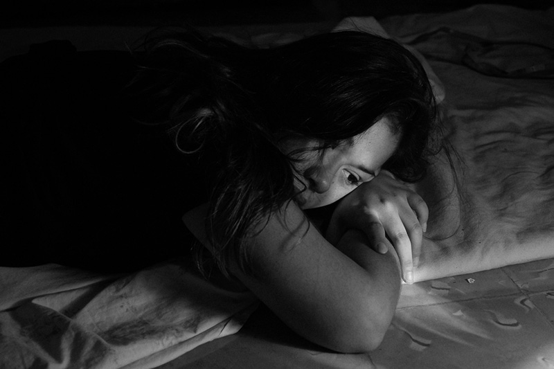 γυναίκα κοιτάζει πίσω από το τζάμι και βιώνει τα σωματικά συμπτώματα της κατάθλιψης