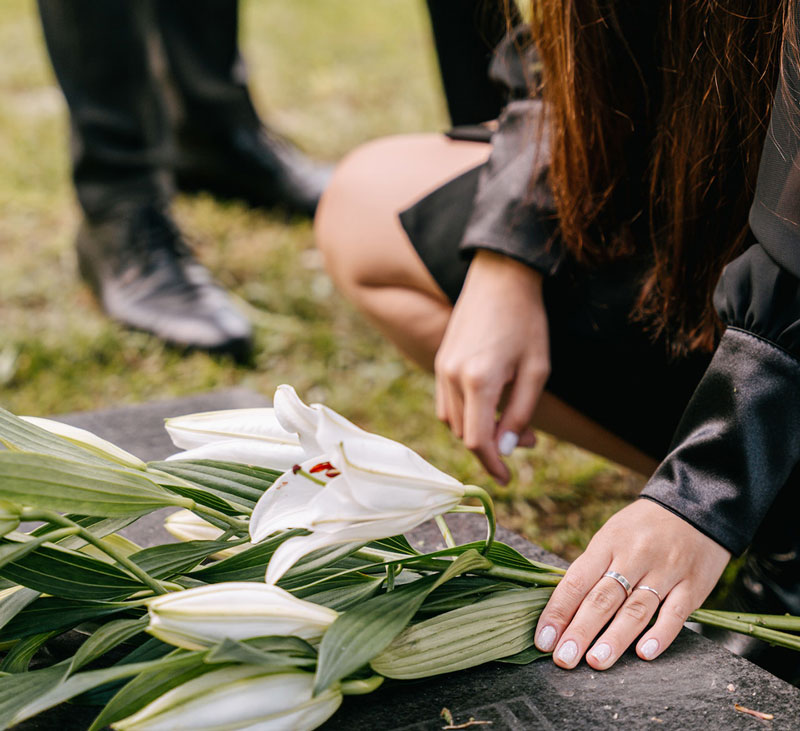 γυναίκα αφήνει λουλούδια σε τάφο αγαπημένου της προσώπου