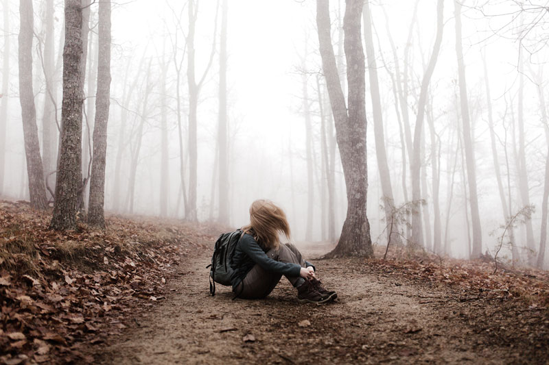μία κοπέλα κάθεται στο έδαφος μέσα σε ένα δάσος
