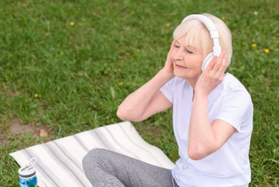 ηλικιωμένη γυναίκα που ακούει μουσική καθισμένη στο γρασίδι