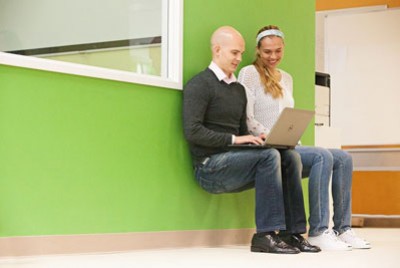 άνδρας και γυναίκα στέκονται σε ένα τοίχο κοιτώντας το laptop