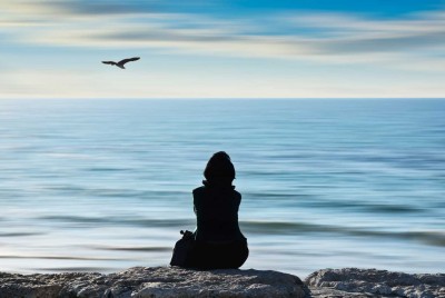 γυναίκα που κάθεται στα βράχια και ατενίζει τη θάλασσα