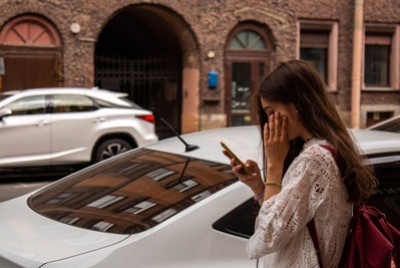 νεαρή κοπέλα διαβάζει μηνύματα στο κινητό της σε ένα δρόμο