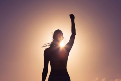 γυναίκα σηκώνει το χέρι της ψηλά με φόντο τον ήλιο