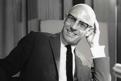 o Michel Foucault με γυαλιά χαμογελάει πιάνοντας το κεφάλι του