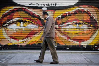 άντρας μεσήλικος περπατάει στην πόλη μπροστά από ένα γκράφιτι