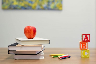 ένα θρανίο με ένα μήλο πάνω σε διάφορα βιβλία και χρωματιστά μολύβια