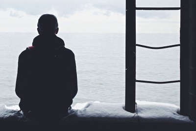 άντρας κάθεται σε ένα χιονισμένο παράθυρο και βλέπει τη θάλασσα