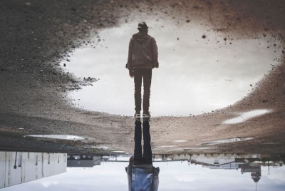 φωτογραφία άντρα που στέκεται πάνω από μια λακούβα με νερό και φαίνεται η αντανάκλασή του