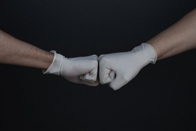 χέρια δύο ανθρώπων με γάντια κάνουν χειρονομία αλληλεγγύης γιατί οι αρετές δεν είναι νόσοι για να μεταδοθούν