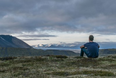 άντρας κάθεται στο γρασίδι αγναντεύοντας τα βουνά