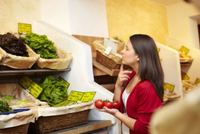 γυναίκα στο σούπερ μάρκετ σκέφτεται τι λαχανικά θα αγοράσει