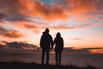 ζευγάρι πιασμένο χέρι χέρι βλέπει το ηλιοβασίλεμα