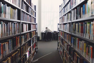 διάδρομος σε βιβλιοθήκη που δείχνει στο βάθος ένα αγόρι να διαβάζει σε γραφείο