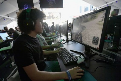 έφηβος που παίζει διαδικτυακά παιχνίδια στον υπολογιστή του σε μία αίθουσα με άλλους εφήβους