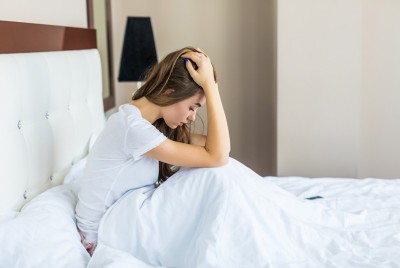 γυναίκα που πάσχει από αϋπνία που οφείλεται στο άγχος είναι καθισμένη σε κρεβάτι και ανησυχεί