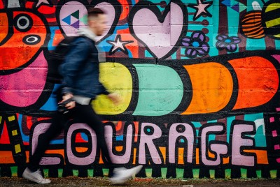 νέος άνδρας με μπουφάν και τσάντα περπατά μπροστά από έναν τοίχο με γκράφιτι αναρωτιέται γιατί είναι τόσο δύσκολο να αλλάξει