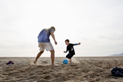 πατέρας και γιος παίζουν μπάλα σε παραλία το ηλιοβασίλεμα