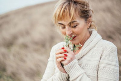 γυναίκα που μυρίζει ένα λουλούδι που κρατά στο χέρι της έχει θετική επίδραση από τις συνήθειές της στην ψυχική της υγεία
