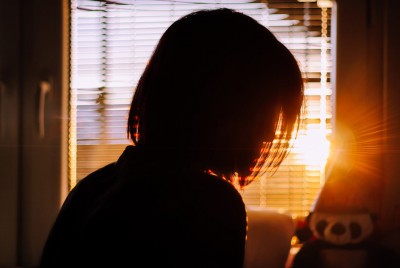 γυναίκα μέσα στο σπίτι της πίσω από το τζάμι με ηλιοβασίλεμα