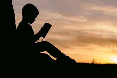 μία παιδική σιλουέτα κάθεται και διαβάζει ένα βιβλίο στο ηλιοβασίλεμα