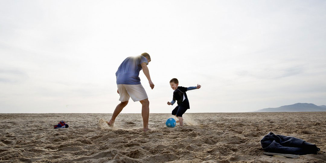 πατέρας και γιος παίζουν μπάλα σε παραλία το ηλιοβασίλεμα