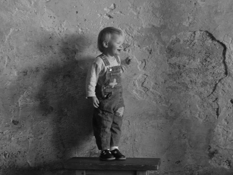 ασπρόμαυρη φωτογραφία που απεικονίζει ένα αγοράκι να στέκεται δίπλα σε έναν φθαρμένο τοίχο