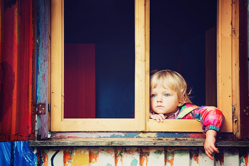 παιδί που στέκεται σε ένα παράθυρο ξύλινου σπιτιού και κοιτάζει προς τα έξω