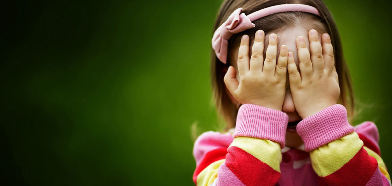 κοριτσάκι με χρωματιστή μπλούζα που κλείνει τα μάτια με τα χέρια της γιατί ντρέπεται