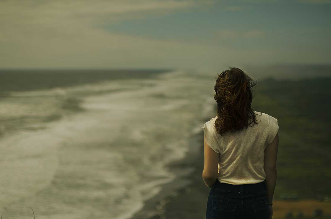 γυναίκα περπατάει στην παραλία με κύμα στη θάλασσα και κάνει την σωστή αυτοκριτική