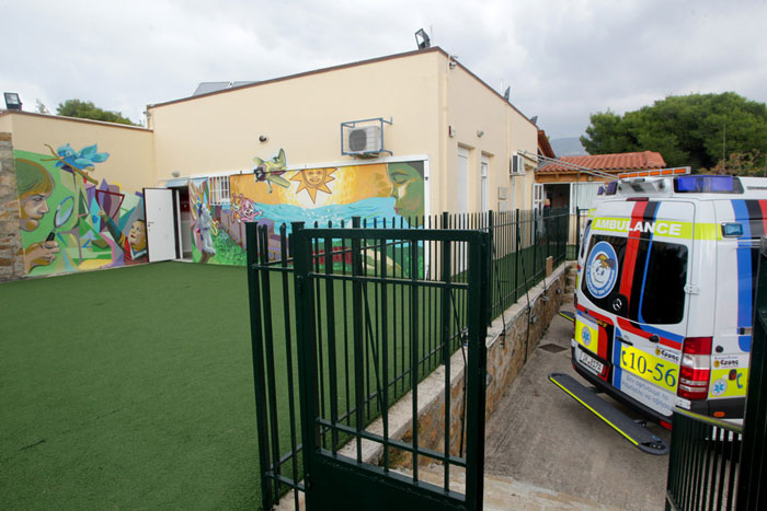 ασθενοφόρο του χαμόγελου του παιδιού μπροστά από ένα σχολείο με πράσινη αυλή