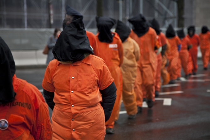 φυλακισμένοι με πορτοκαλί στολές και κουκούλες βαδίζουν σε μία σειρά